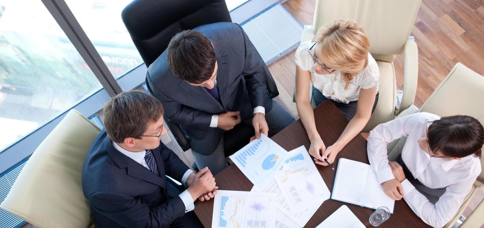 Top down view of a group of consultants at a meeting table with papers and graphs in front of them